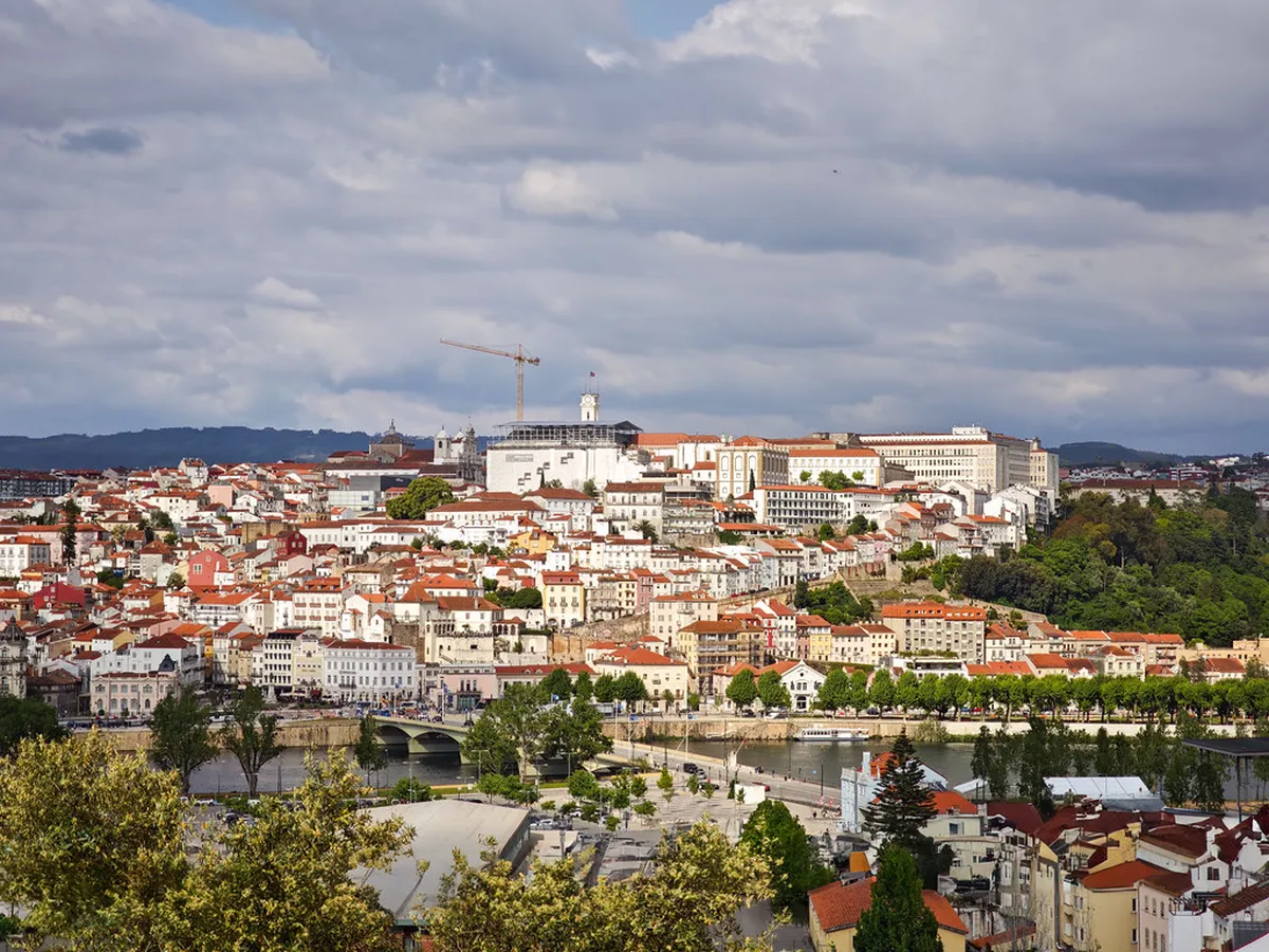 Sweeping panoramic view of Coimbra's historic rooftops and the Mondego River from a hillside miradouro