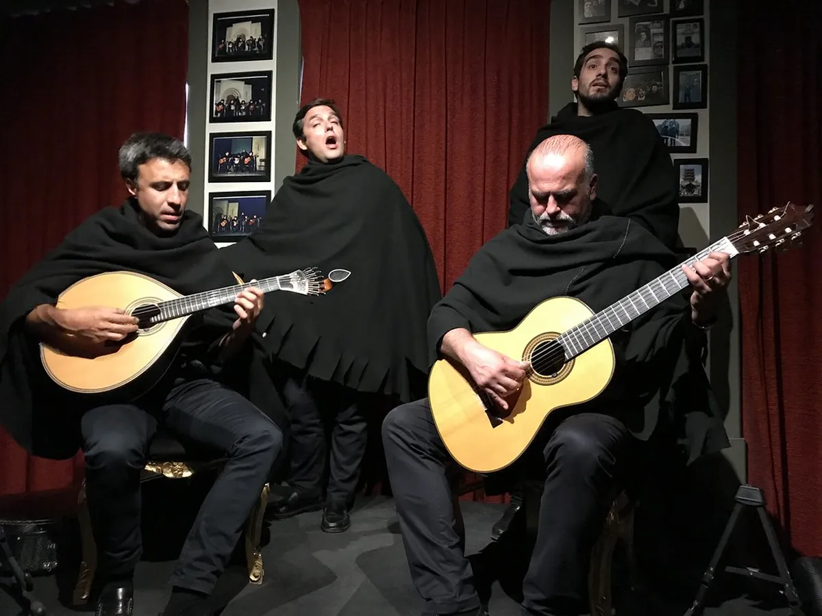 A Coimbra Fado performance with a singer in traditional academic cape playing guitar in a dimly lit historic venue