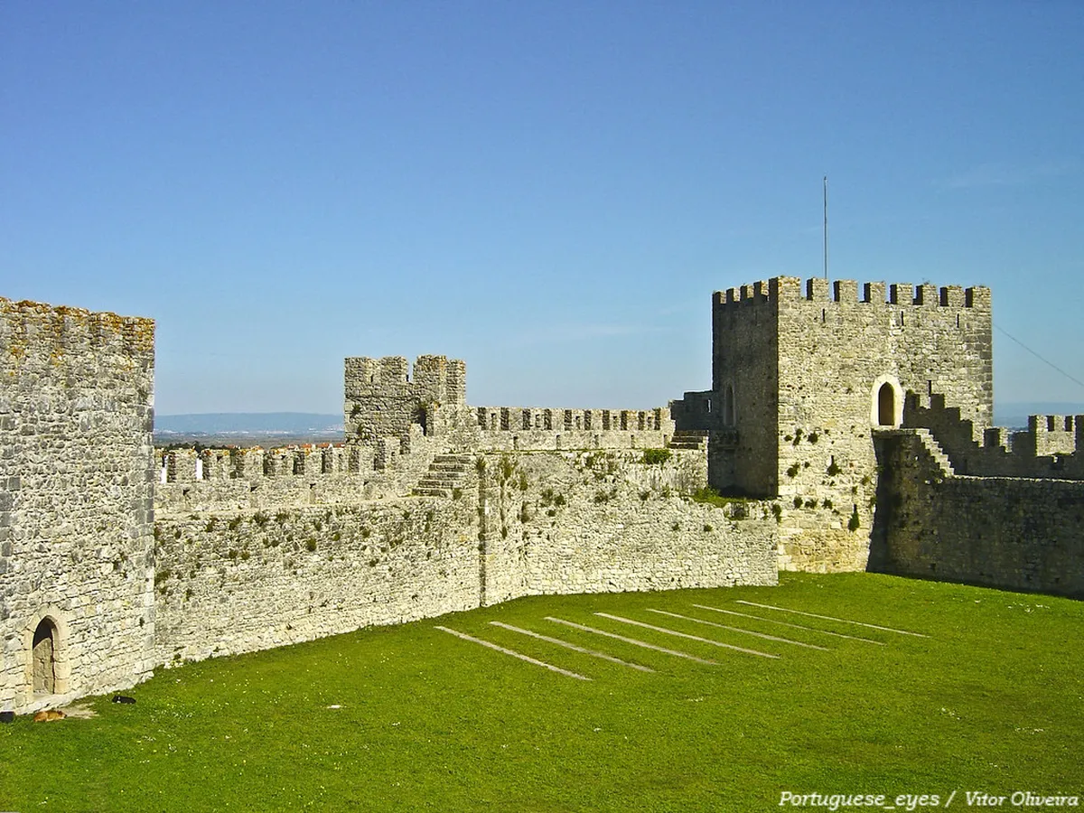 Medieval stone walls and towers of Coimbra rising above the Mondego River, reflecting centuries of fortification history