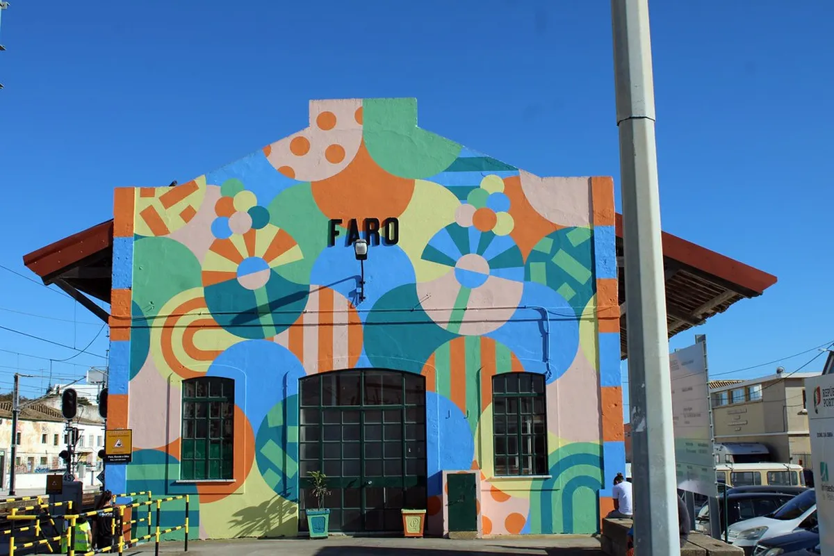 Large-scale urban mural painted on a whitewashed wall in Faro, Portugal, showcasing vibrant contemporary art