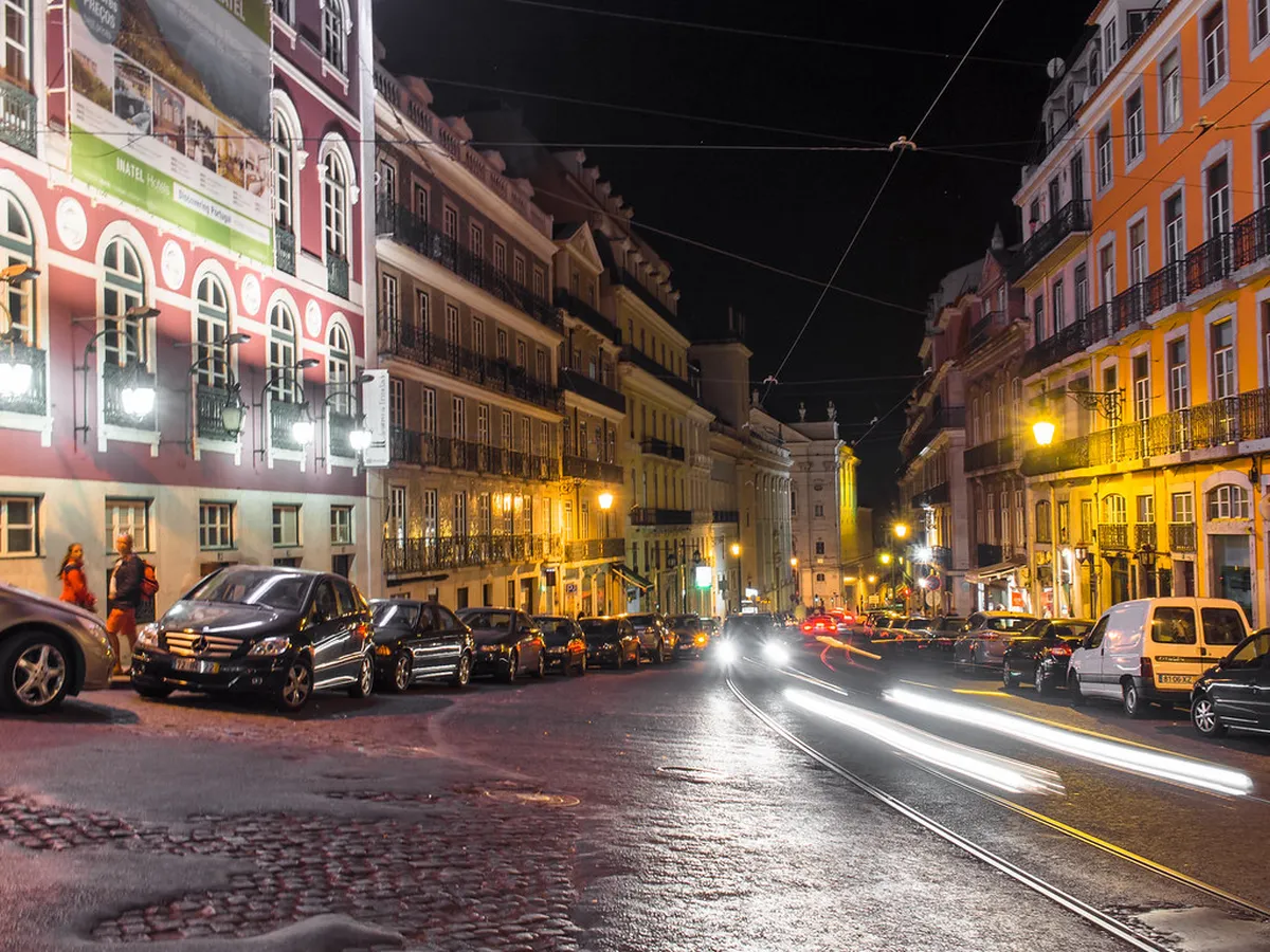 Steep Lisbon cobblestone street at night with warm lamplight reflecting off the traditional calçada pavement
