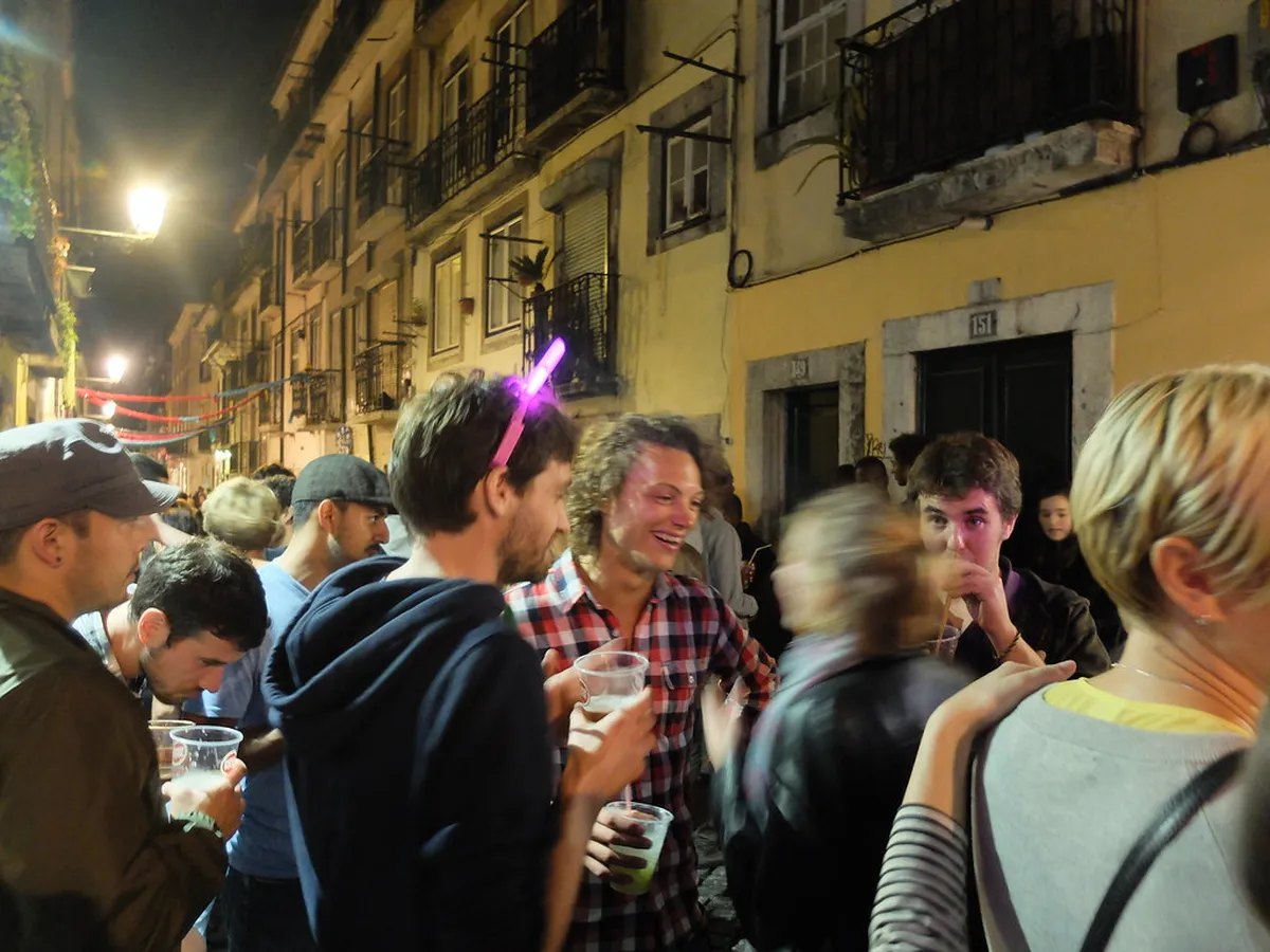 Lisbon Bairro Alto narrow cobblestone street lined with small bars and glowing neon signs at night