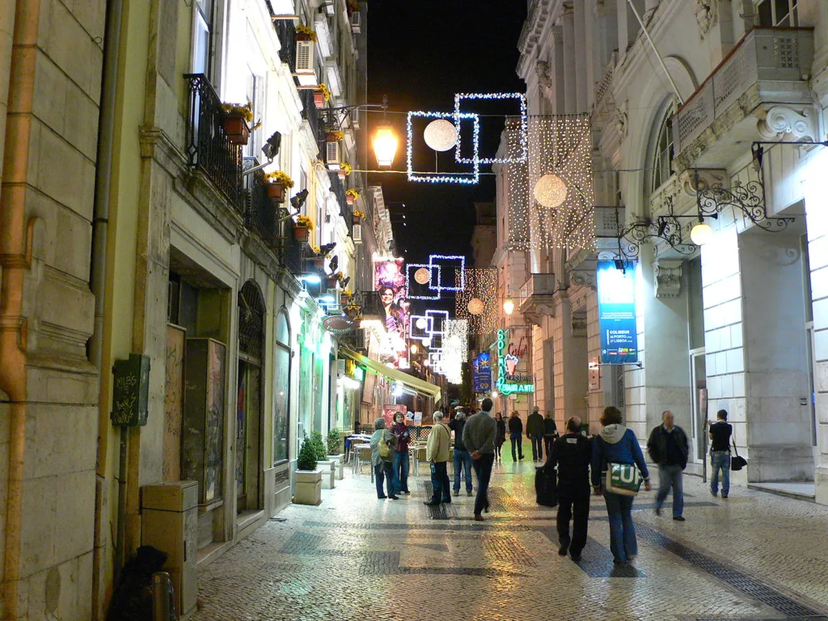 Lisbon's Rua das Portas de Santo Antão bustling with outdoor restaurant tables and evening diners
