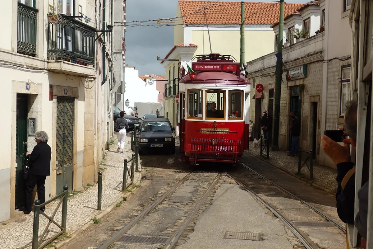 A vintage yellow Remodelado tram navigating a narrow Lisbon street in the Alfama district