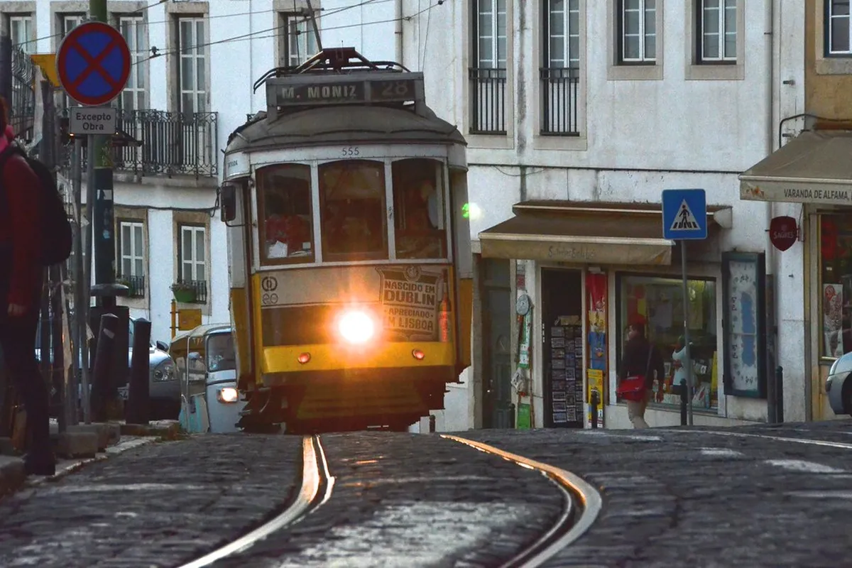 Lisbon Tram 28 yellow carriage navigating a quiet cobblestone street on a weekday morning