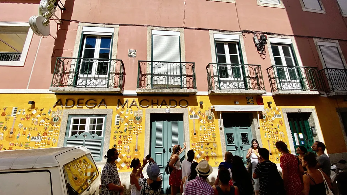 Lively Lisbon Bairro Alto street scene at dusk with fado bar signs and locals gathering outside tascas