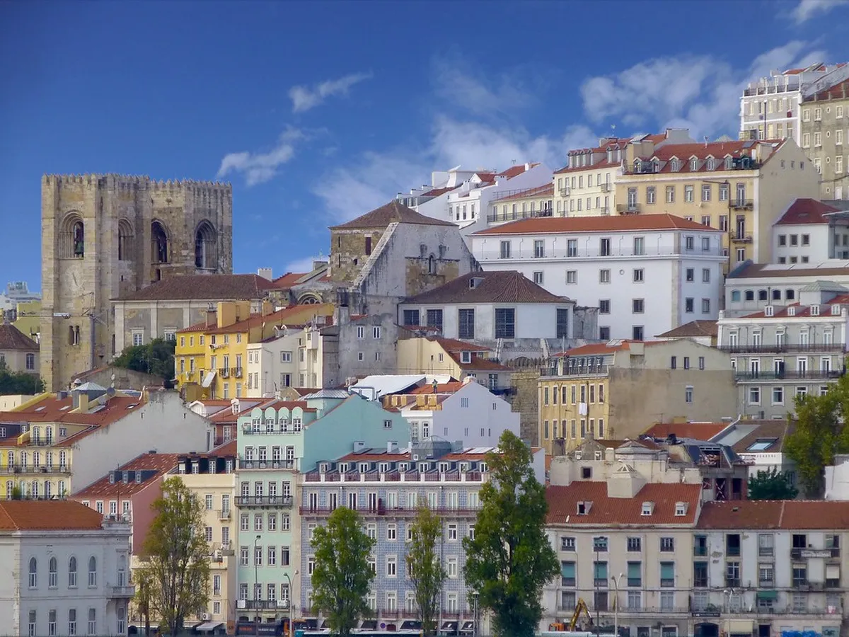 Narrow cobblestone alley winding through Lisbon's Alfama neighbourhood with colourful tiled buildings