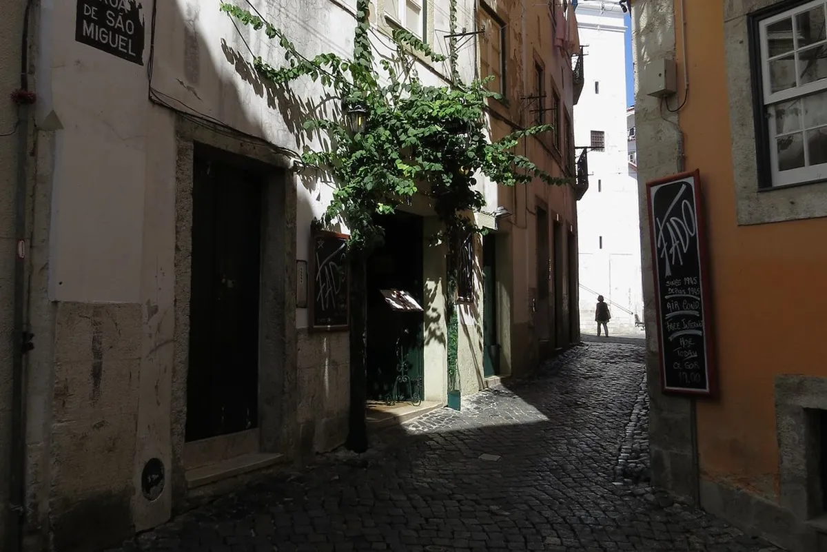 Narrow cobblestone alley winding through Lisbon's Alfama district with colourful tiled buildings on either side