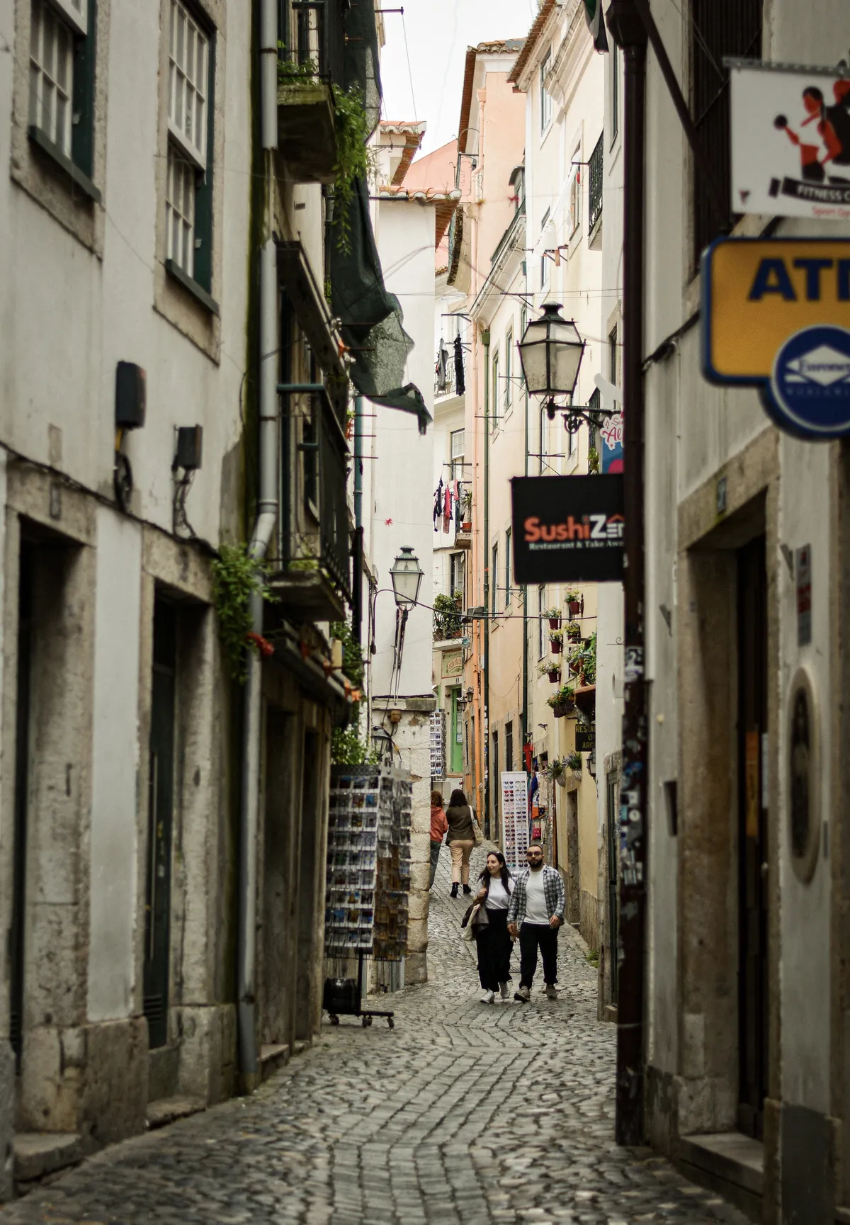Sunlit cobblestone alleyway in Lisbon's Graça district lined with traditional azulejo-tiled buildings