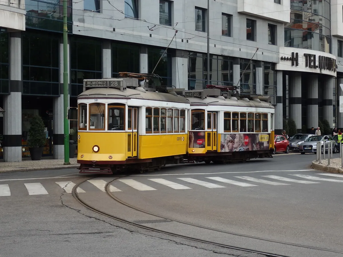 Lisbon Tram 28 stop with passengers queuing to board the historic yellow streetcar on a sunny day