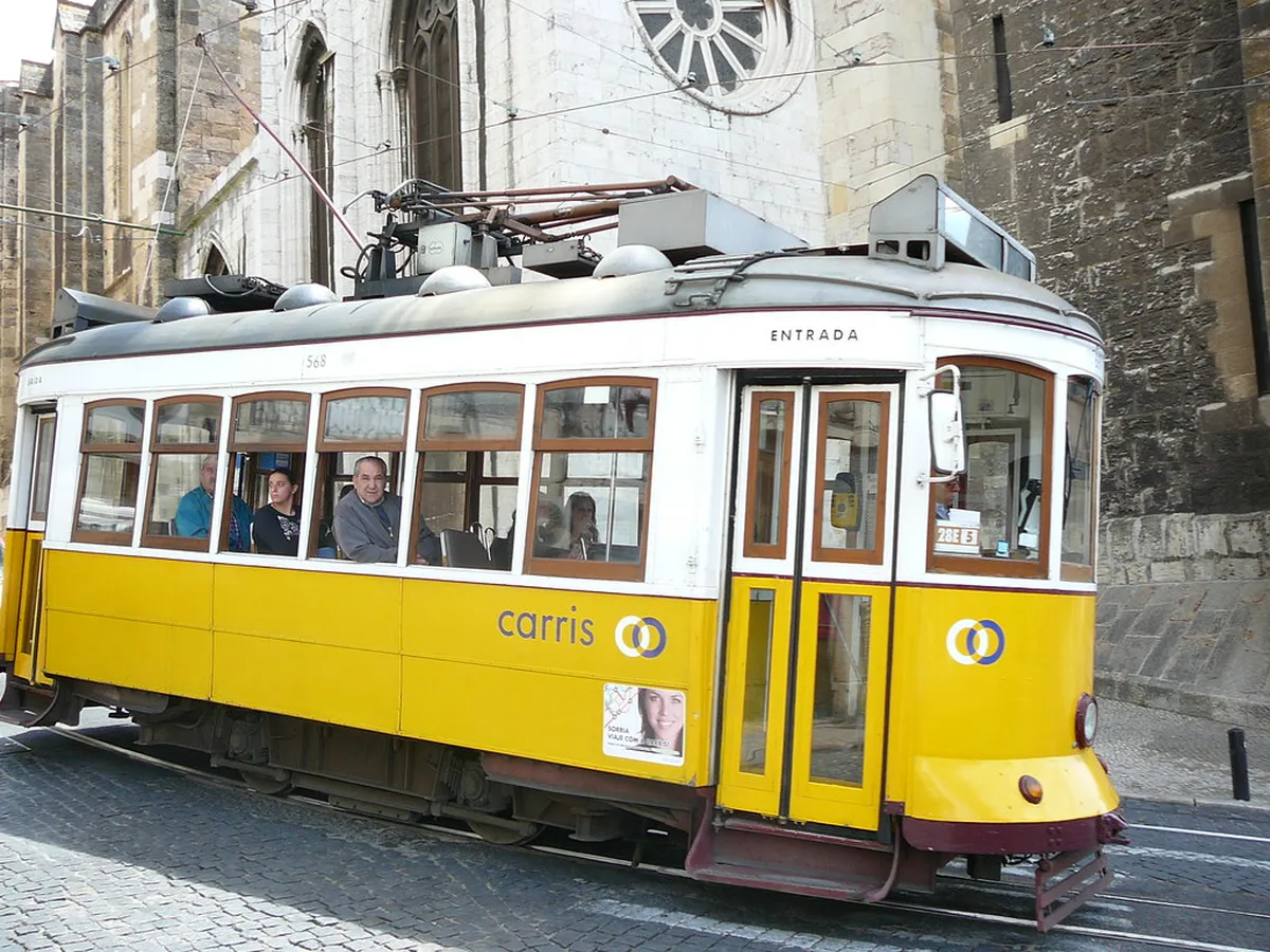 Lisbon's iconic yellow Tram 28 rattling through narrow cobblestone streets lined with tiled buildings