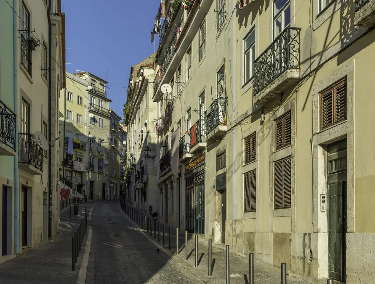 Lisbon Alfama cobblestone street winding between traditional pastel-coloured houses with tiled facades