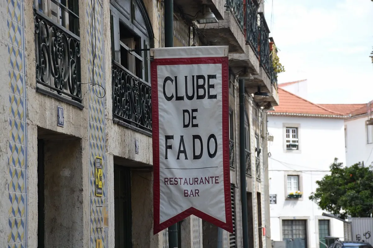 Lisbon Alfama district narrow cobblestone alley with colourful facades leading toward the iconic Clube de Fado venue