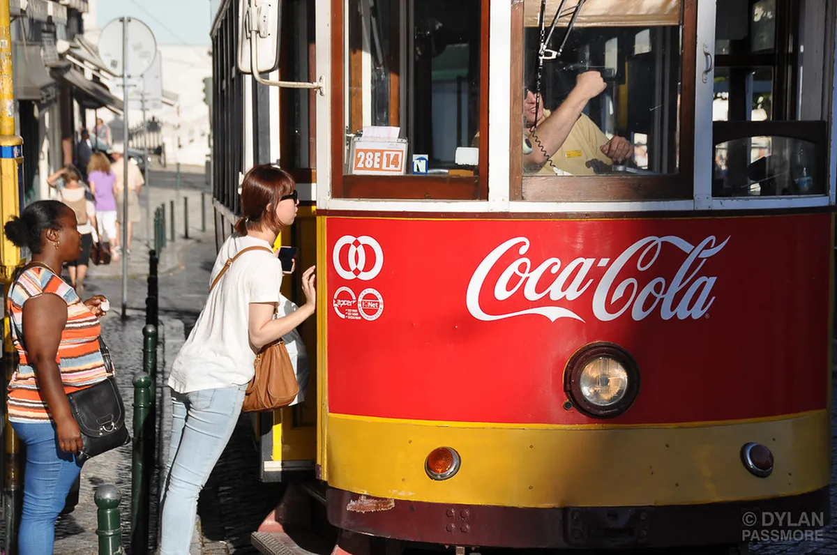 Passengers boarding a yellow Lisbon tram at a busy stop, with a crowd pressing toward the doors