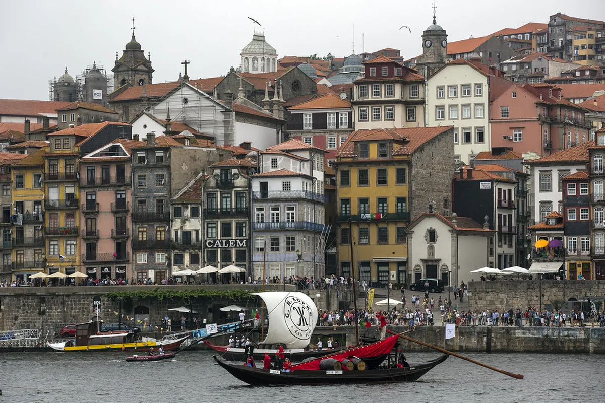 Traditional rabelo boats carrying wine barrels along the Porto Douro River with colorful waterfront buildings reflected in the water