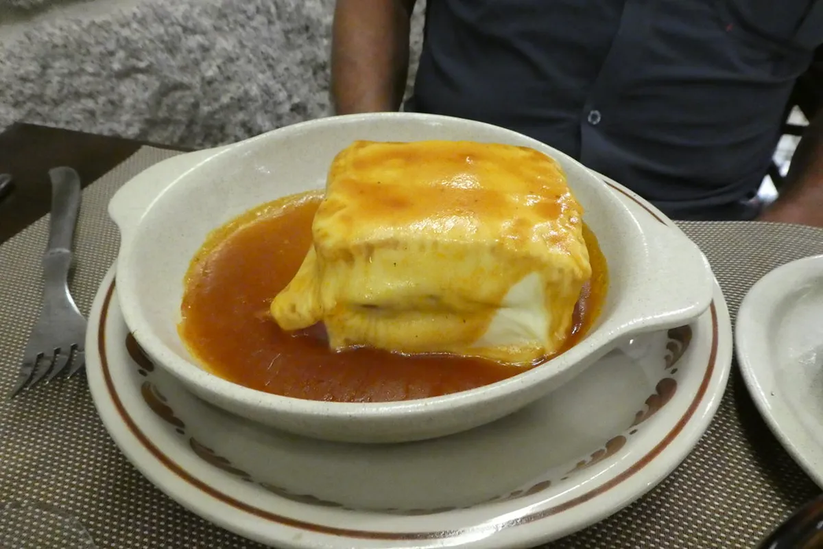 A classic Porto Francesinha sandwich smothered in rich tomato-beer sauce and melted cheese, served at a Ribeira restaurant